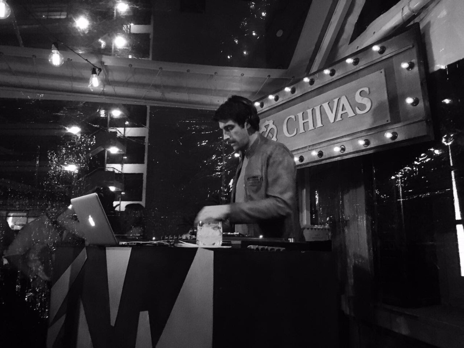 Pedro Etcheverry musicalizando bajo el cartel luminoso de Chivas Regal en evento de marca, fotografía en blanco y negro