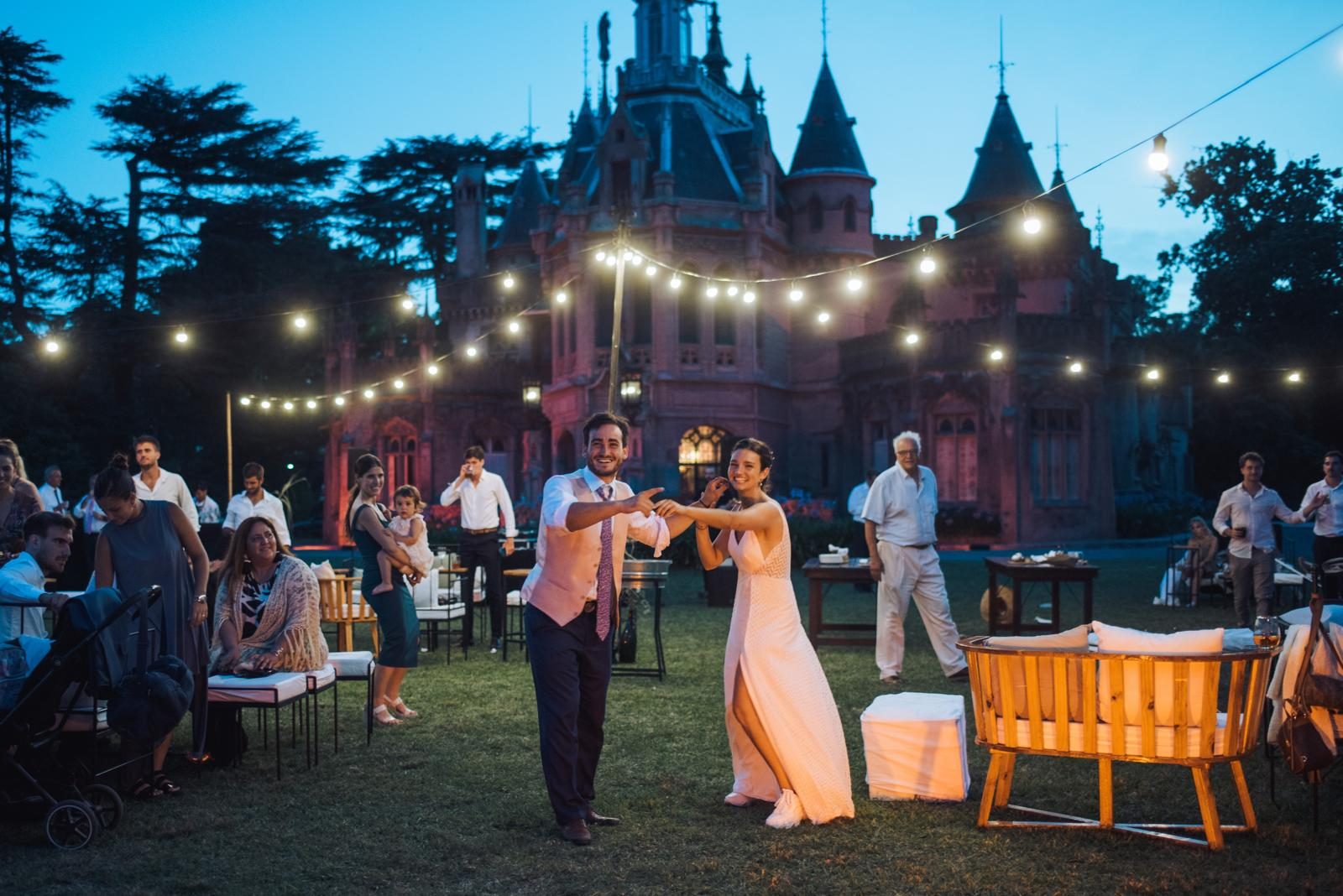 Novios bailando bajo las guirnaldas de luces frente al castillo en su casamiento al aire libre