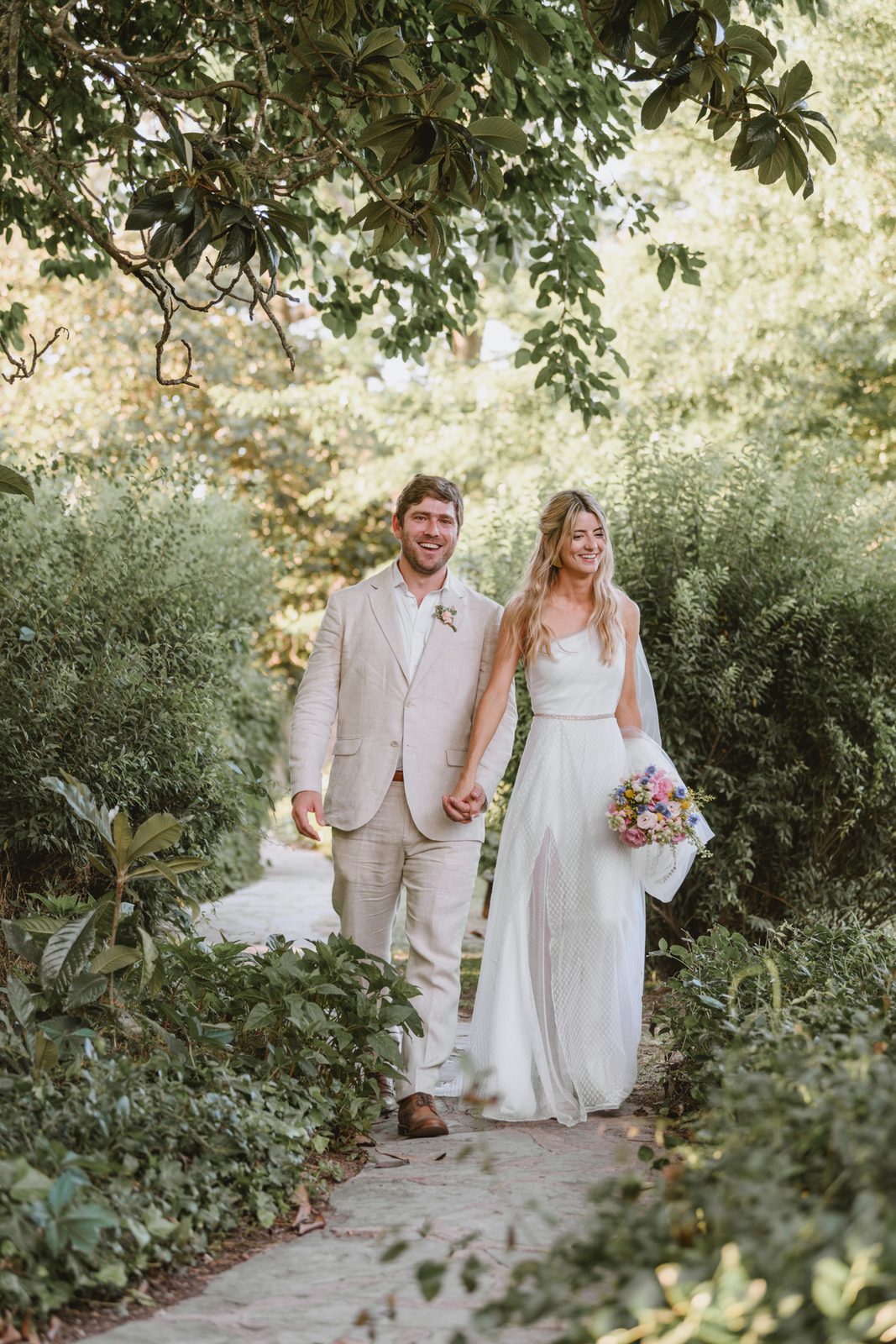 Pareja de novios sonriendo por el sendero del jardín de una estancia en su casamiento al aire libre